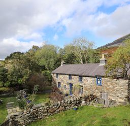A stone cottage with blue windows and a fenced garden with a picnic table at Llwyn Bedw in Nant Peris