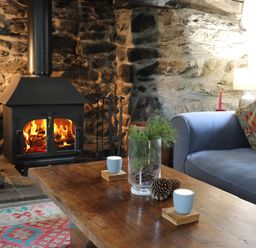 A living room with a wood burning stove a blue sofa with patterned cushions and a wooden coffee table with candles and pine cones at Llwyn Bedw in Nant Peris