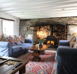 A living room with blue sofas patterned cushions a wooden coffee table and a wood burning stove in a stone fireplace at Llwyn Bedw in Nant Peris