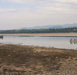 A view of a boat on the water near a pier with mountains in the background at Menai Cottage in Brynsiencyn
