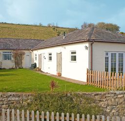 A single story house with white walls and a garden with grass and a wooden fence at Mermaid Cottage in Brynsiencyn