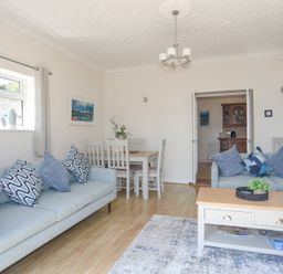 A living room with two sofas a coffee table a dining table with chairs and a chandelier at Mermaid Cottage Brynsiencyn