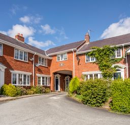 A row of brick townhouses with white-framed windows and doors surrounded by shrubs and bushes at Mews Cottage in Menai Bridge