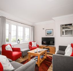 A living room with red and grey chairs a wooden coffee table a television and a mirror at Mews Cottage in Menai Bridge