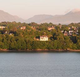 A view of a river with trees and houses on the opposite bank and mountains in the background at Mews Cottage in Menai Bridge