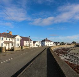 A road running alongside a row of houses and a beach with seaweed at Min Y Mor Trearddur Bay in Trearddur Bay