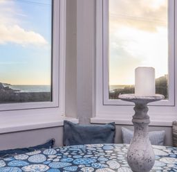 A table with a candle holder and cushions by two windows overlooking the sea at Min Y Mor Trearddur Bay in Trearddur Bay