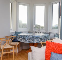 A dining area with a round table covered with a blue patterned tablecloth surrounded by wooden chairs and cushions at Min Y Mor Trearddur Bay