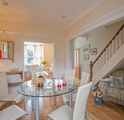 A dining room with a glass table and six white chairs next to a staircase and a wooden floor at Morfin in Criccieth