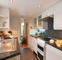 A kitchen with a stainless steel sink white cabinets a stove with a toaster carrots and bread at Morfin in Criccieth
