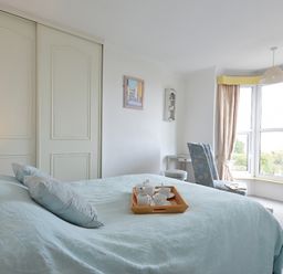 A bedroom with a bed and tea set on a tray by a window with curtains and an armchair at Morfin in Criccieth