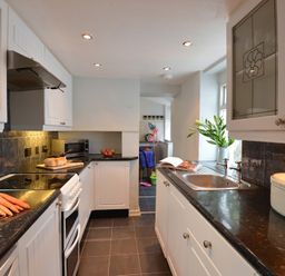 A kitchen with white cabinets black countertops carrots bread and a vase with leaves at Morfin in Criccieth