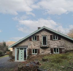 A stone house with green window frames and shutters surrounded by trees and grass at Morfa Lodge in Porthmadog