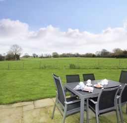An outdoor patio with a dining table and six chairs overlooking a grassy fenced field at Mynydd Parys in Brynsiencyn