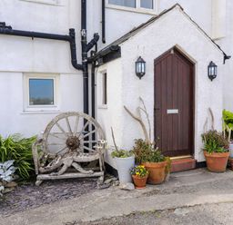 An entrance door with potted plants and an old wooden wagon wheel bench outside at Pant yr Hyman in Rhoscolyn