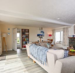A living room with beige sofas a blue checkered throw a wooden coffee table and a stone fireplace at Pant yr Hyman in Rhoscolyn