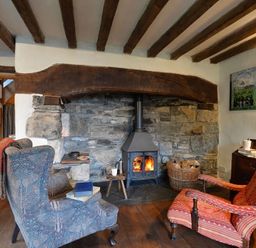A room with two armchairs a wood burning stove and a basket of firewood at Pantlleni in Nant Gwynant