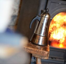 A metal coffee pot on a wooden stool in front of a burning fireplace at Pantlleni in Nant Gwynant