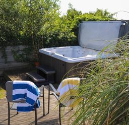 An outdoor area with a hot tub, two chairs with towels, and surrounding greenery at Pencraig in Trearddur Bay