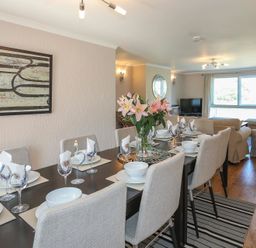 A dining area with a set table and a seating area with sofas and a television at Pencraig in Trearddur Bay