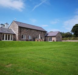 A stone house with multiple windows and patio furniture on a lawn at Penrhyn Barn in Dulas