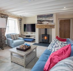 A living room with blue chairs a wooden coffee table a chess set a fireplace and a television at Penrhyn Barn in Dulas