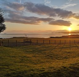 A grassy field with a wooden fence overlooking the sea at sunset at Penrhyn Barn in Dulas