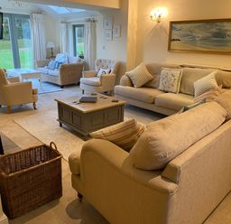 A living room with beige sofas a wooden coffee table and large windows at Penrhyn Farm in Moelfre