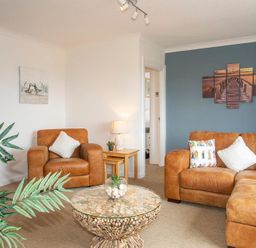 A living room with brown leather sofas a round wooden coffee table lamp and wall art at Pen Y Daith in Aberffraw