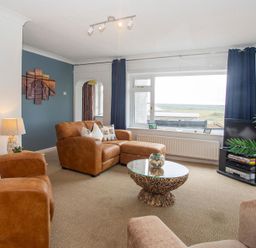 A living room with brown armchairs and a glass coffee table near a large window at Pen Y Daith in Aberffraw