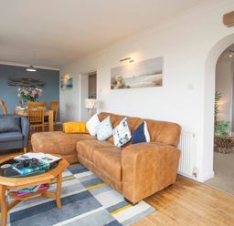 A living room with a brown sofa blue armchair wooden dining table and chairs at Pen Y Daith in Aberffraw
