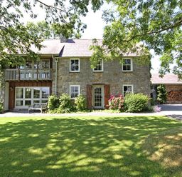 A stone house with wooden shutters and balcony surrounded by green lawn and trees at Perth Hwfa in Malltraeth