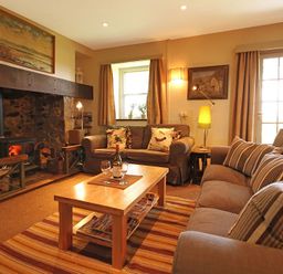 A living room with two sofas a wooden coffee table a fireplace and a lamp at Perth Hwfa in Malltraeth