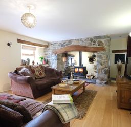 A living room with sofas a wooden coffee table a stone fireplace and a television at Pen Y Bont in Pontllyfni