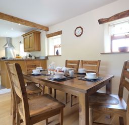 A wooden dining table set with bowls cups and eggs in a kitchen with wooden cabinets and beams at Pen Y Bont in Pontllyfni