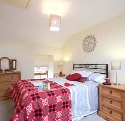 A bedroom with a double bed with pillows and a patterned blanket with wooden dressers and lamps at Pen Y Bont in Pontllyfni