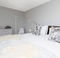A bedroom with a double bed white and patterned pillows a white dresser with folded towels a white chair and a coat rack at Rhyd Angharad Barns in Rhydwyn