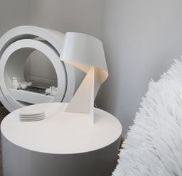 A round white side table with a modern white lamp and coasters beside a white fluffy chair and circular fireplace in Rhyd Angharad Barns in Rhydwyn