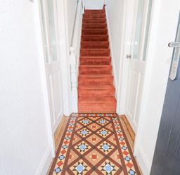 A hallway with patterned tiled floor and red carpeted stairs at Seiriol View in Moelfre