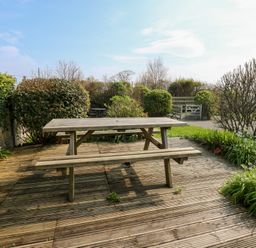 A wooden picnic table on a wooden deck surrounded by bushes and plants at Seiriol View in Moelfre