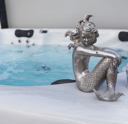 A silver mermaid statue on the edge of a hot tub with blue water and two blue candles at The Mermaid in Brynsiencyn