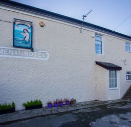 Exterior view of a building with sign Menai Hotel and Mermaid Inn with windows stairs and flower pots at The Mermaid in Brynsiencyn