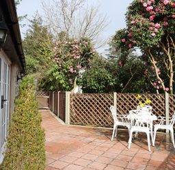 An outdoor patio with white metal table and four chairs surrounded by a brown lattice fence and flowering trees at The Honey Pot in Garndolbenmaen