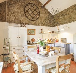 A kitchen with a wooden table and chairs a white refrigerator and stone walls at Three Gates in Llangoed