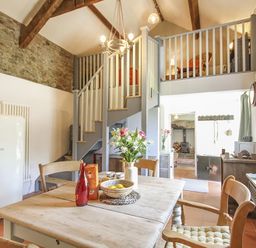 A kitchen dining area with wooden table chairs flowers and a bowl of fruit under exposed beams at Three Gates in Llangoed