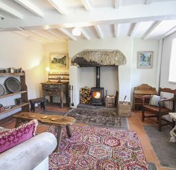 A living room with a wood burning stove wooden furniture and shelves with pewter plates and mugs at Three Gates in Llangoed