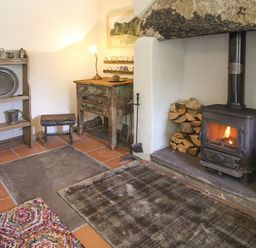 A room with a wood burning stove a small wooden table shelves with metal dishes and a wooden stool at Three Gates in Llangoed