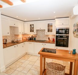 A kitchen with white cabinets a wooden table and tiled floor at The Little Coach House in Garndolbenmaen