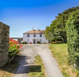 A driveway leading to a white two-story house with flowers and trees at Towyn Lodge in Trearddur Bay