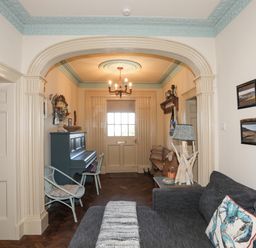A living room with a gray sofa and a piano near the door at Towyn Lodge in Trearddur Bay